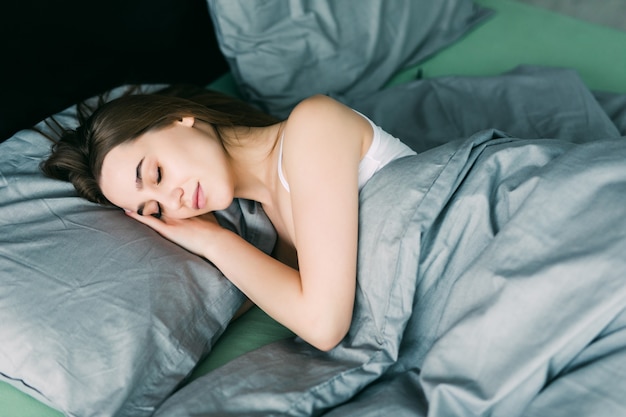 Mujer hermosa joven durmiendo en su cama vista superior