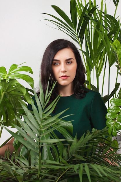 Mujer hermosa joven emplazamiento entre grandes plantas caseras