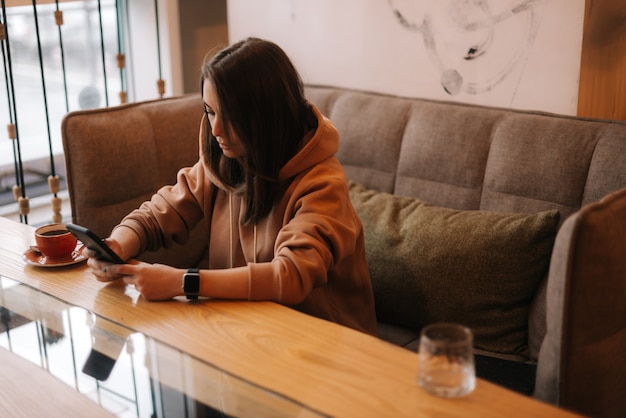 Mujer hermosa joven escribiendo un mensaje en el teléfono en la acogedora cafetería