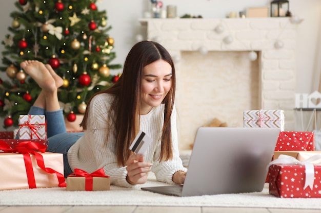 Mujer hermosa joven está comprando para la Navidad en el interior festivo en casa