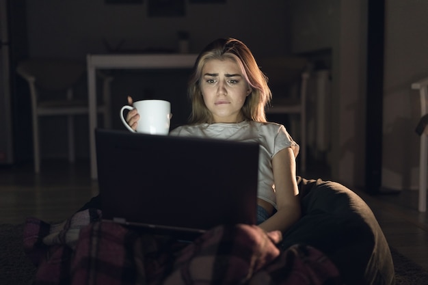 Mujer hermosa joven está sentada en casa sola y viendo un thriller