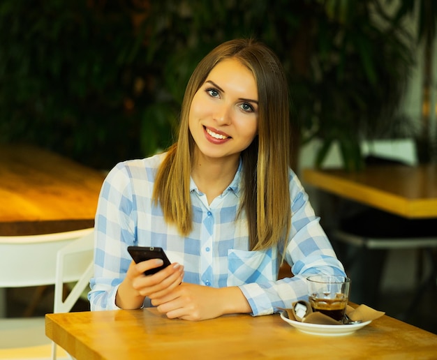 Mujer hermosa joven está tomando café y leyendo las noticias de la mañana por el teléfono móvil