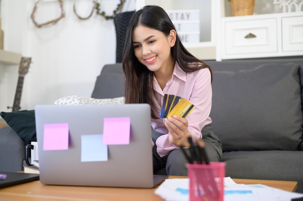Una mujer hermosa joven está utilizando tarjeta de crédito para compras en línea en el sitio web de Internet en casa, concepto de comercio electrónico