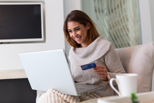 Mujer hermosa joven feliz por encontrar artículos de compra a la venta en línea. Hermosa chica con ordenador portátil para compras en línea en casa