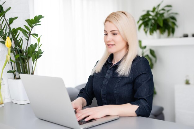 Mujer hermosa joven feliz que usa la computadora portátil, en interiores.