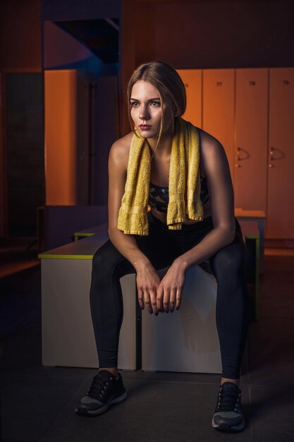 Mujer hermosa joven fitness con toalla descansando en el vestidor. Vestido con ropa deportiva. Gimnasia