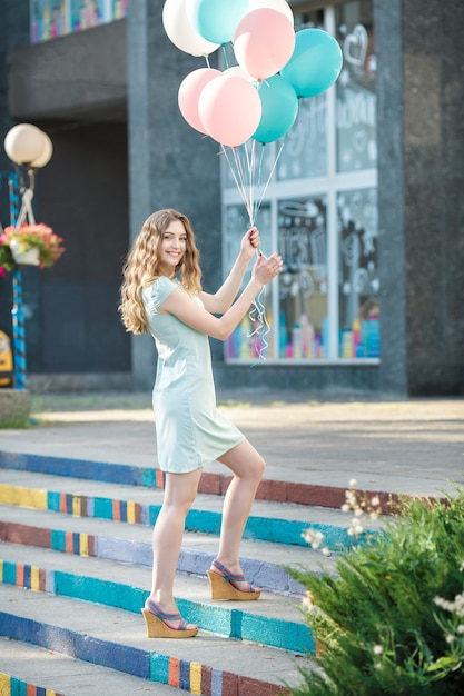 Mujer hermosa joven con globos multicolores volando en la ciudad