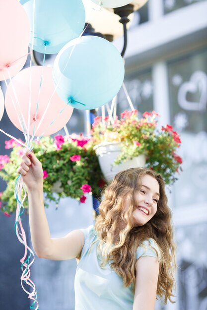 Mujer hermosa joven con globos multicolores volando en la ciudad