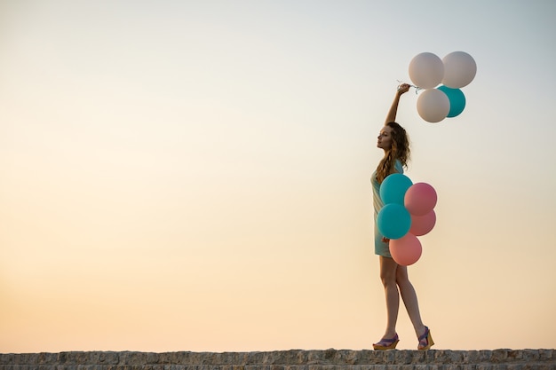 Mujer hermosa joven con globos multicolores volando contra el cielo. concepto de felicidad y sueños