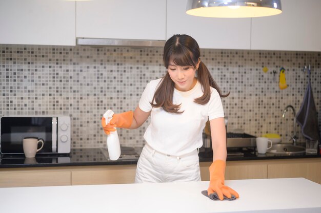 Una mujer hermosa joven con guantes de goma protectores está limpiando la mesa en la cocina de casa.