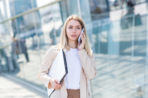 Mujer hermosa joven hablando por un teléfono celular cerca de la oficina, una mujer de negocios en una pausa para el almuerzo