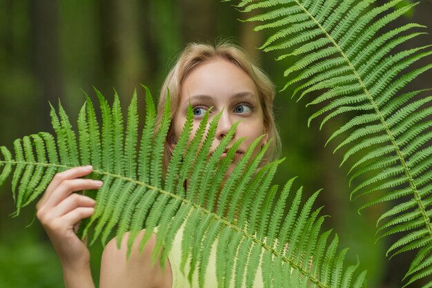 Foto mujer hermosa joven entre las hojas de helecho en el bosque