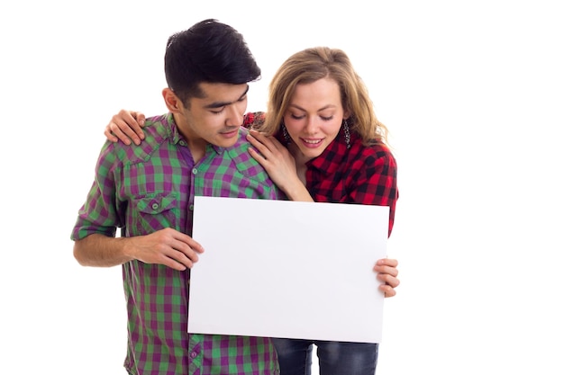 Mujer hermosa joven con un hombre joven y agradable con cabello oscuro en camisas a cuadros sosteniendo un cartel blanco