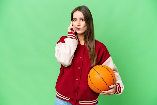 Mujer hermosa joven jugando baloncesto sobre un fondo clave de croma aislado pensando en una idea