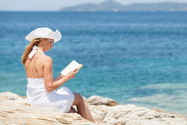 Mujer hermosa joven leyendo un libro y relajándose en la playa.