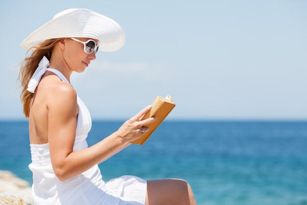 Mujer hermosa joven leyendo un libro y relajándose en la playa.