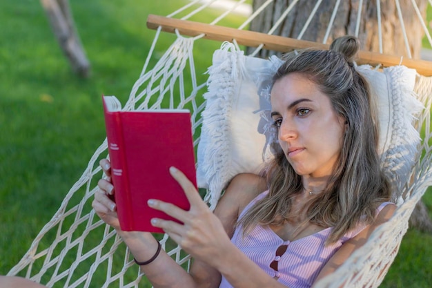 Mujer hermosa joven leyendo un libro relajándose del trabajo en una hamaca al aire libre en la naturaleza