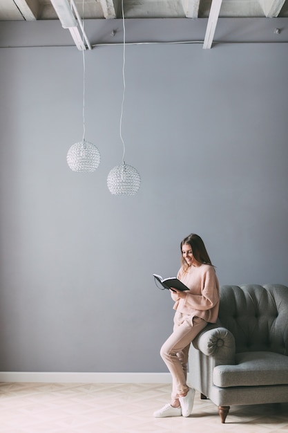 Mujer hermosa joven con un libro junto a la silla en casa.