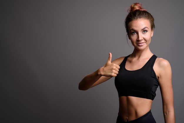 Mujer hermosa joven lista para el gimnasio contra la pared gris