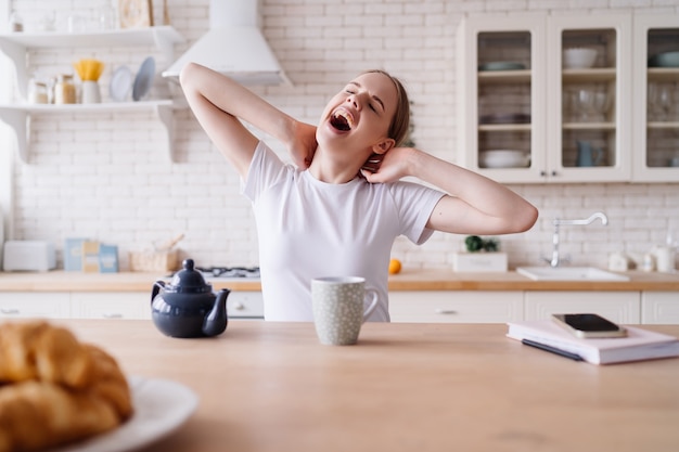 Mujer hermosa joven en la mañana en la cocina con té, estiramiento