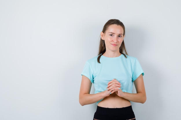 Mujer hermosa joven con las manos entrelazadas frente a sí misma en camiseta y mirando optimista, vista frontal.