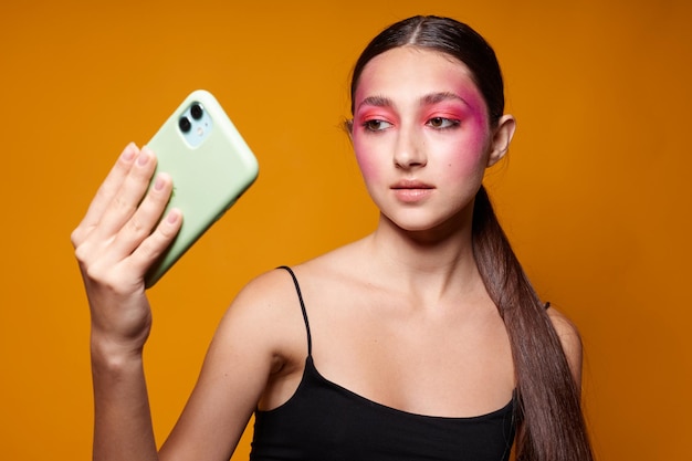 Mujer hermosa joven mira el teléfono maquillaje brillante posando emociones de moda fondo amarillo inalterado. foto de alta calidad