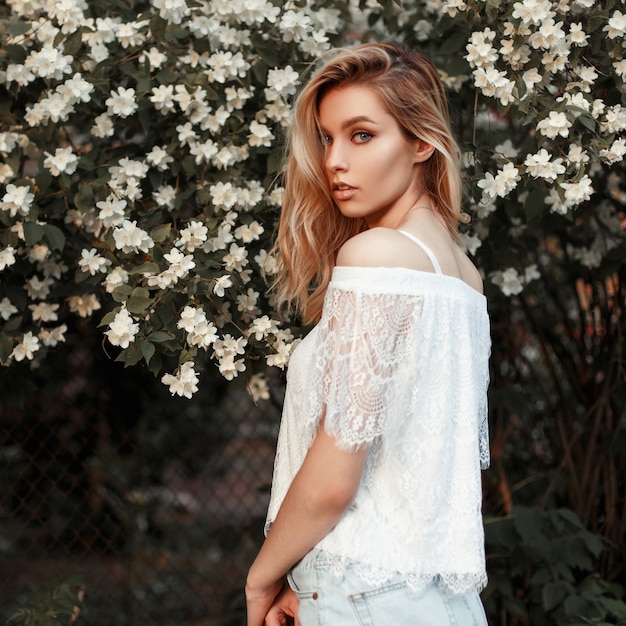 Mujer hermosa joven modelo americano en vestido de encaje blanco cerca de flores