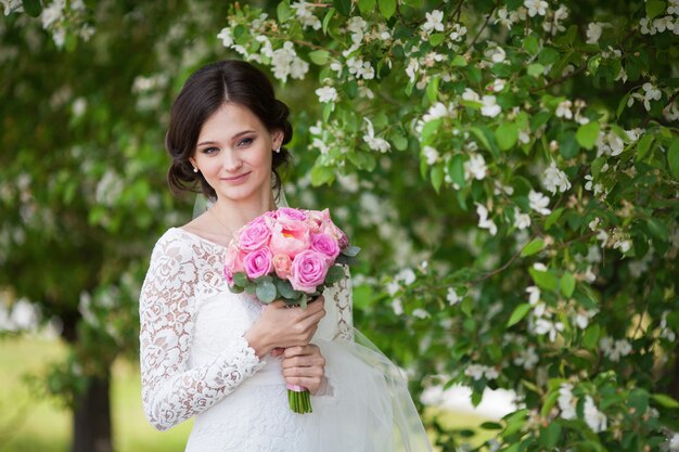 Mujer hermosa joven, novia con ramo de novia en jardín floreciente