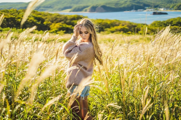 Mujer hermosa joven en el paisaje otoñal con flores secas, espigas de trigo. Moda otoño, invierno. Otoño soleado, suéter acogedor de otoño. foto de moda