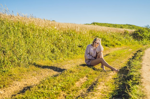 Mujer hermosa joven en el paisaje otoñal con flores secas, espigas de trigo. Moda otoño, invierno. Otoño soleado, suéter acogedor de otoño. foto de moda