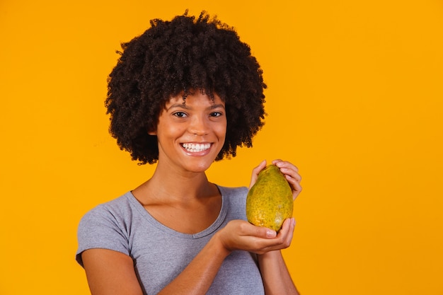 Mujer hermosa joven con papaya en amarillo