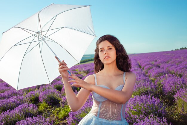 Mujer hermosa joven con paraguas en un campo de lavanda