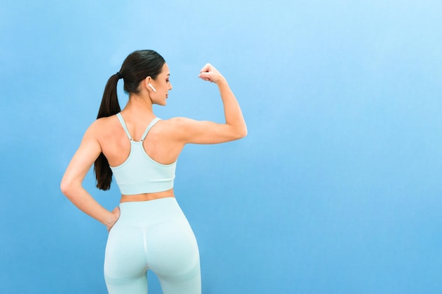 Mujer hermosa joven pasa tiempo en el gimnasio en casa muestra sus músculos sobre un fondo azul Concepto de deporte de entrenamiento