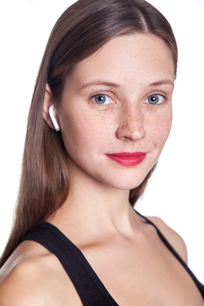 Mujer hermosa joven con pecas y auriculares inalámbricos en las orejas. tiro del estudio.