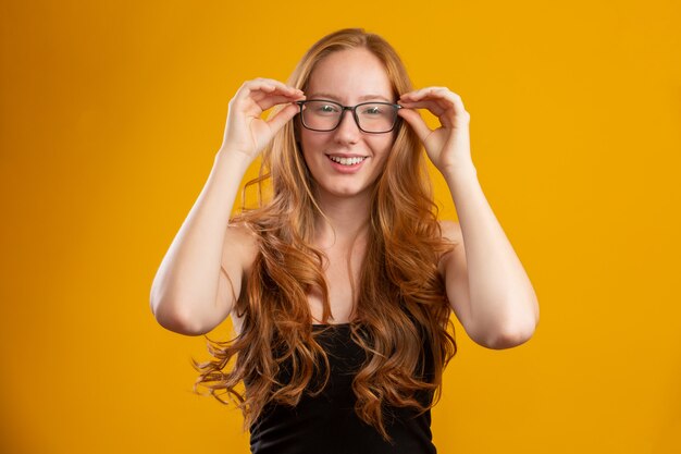 Mujer hermosa joven pelirroja con el pelo rizado feliz con sus gafas. Concepto de cuidado de los ojos.