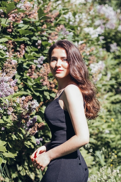 Mujer hermosa joven con pelo largo y rizado morena en vestido negro caminando en el parque de verano