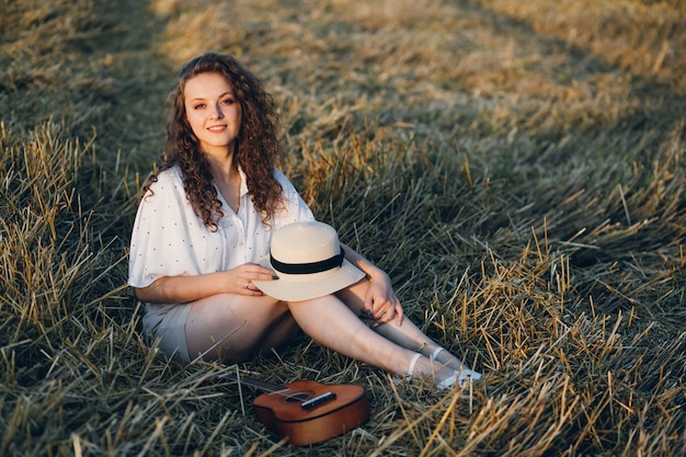 Mujer hermosa joven con el pelo largo y rizado posa en un campo de trigo en el verano al atardecer