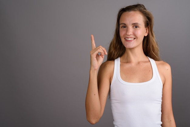 Mujer hermosa joven con el pelo largo y rubio sobre fondo gris