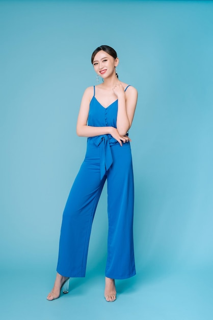 Mujer joven posando en un vestido casual de moda azul con pantalones de cuerpo completo sobre fondo azul | Foto Premium