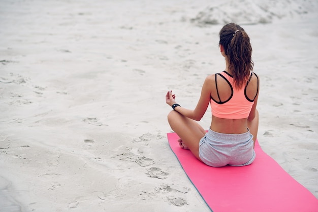 Mujer hermosa joven en posición de loto de manos de yoga en la playa