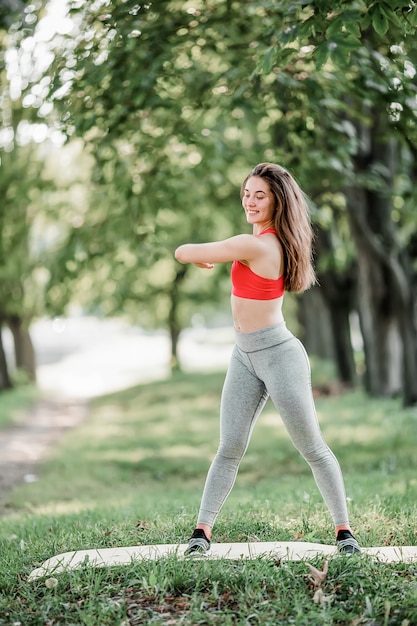 Mujer hermosa joven practicando yoga en el parque verde.