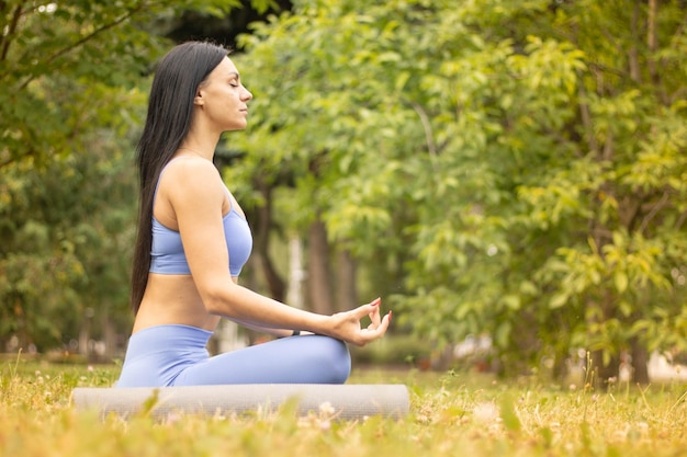 Mujer hermosa joven practicando yoga en el parque.