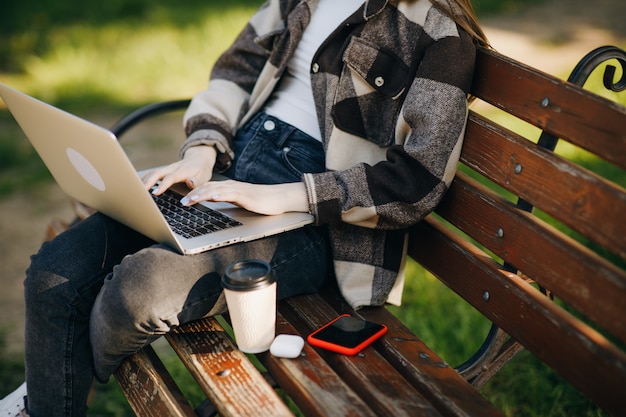 Mujer hermosa joven que se coloca en un banco usando la computadora portátil