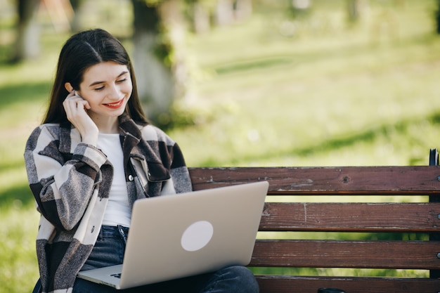 Mujer hermosa joven que se coloca en un banco usando la computadora portátil