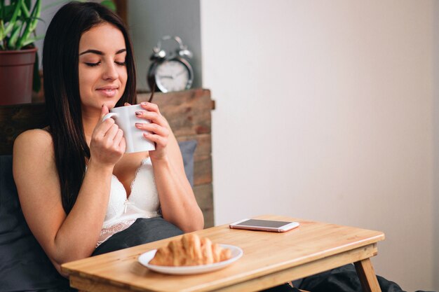 Mujer hermosa joven que desayuna en cama