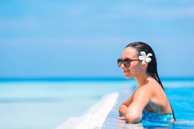 Mujer hermosa joven que disfruta de vacaciones de verano en piscina de lujo