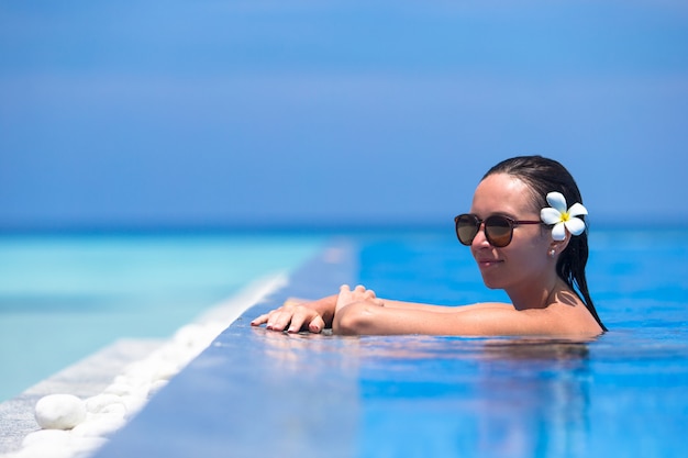 Mujer hermosa joven que disfruta de vacaciones de verano en piscina de lujo