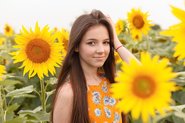 Mujer hermosa joven que disfruta del verano, la juventud y la libertad, sosteniendo girasoles contra el cielo azul. Imagen tonificada.