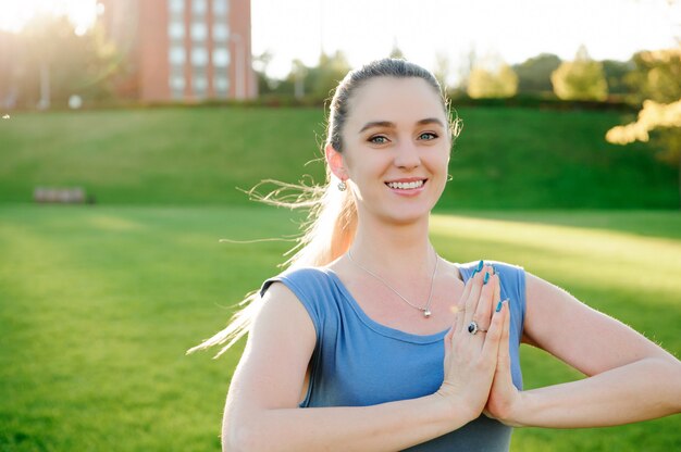 Mujer hermosa joven que hace ejercicios de yoga en el parque.