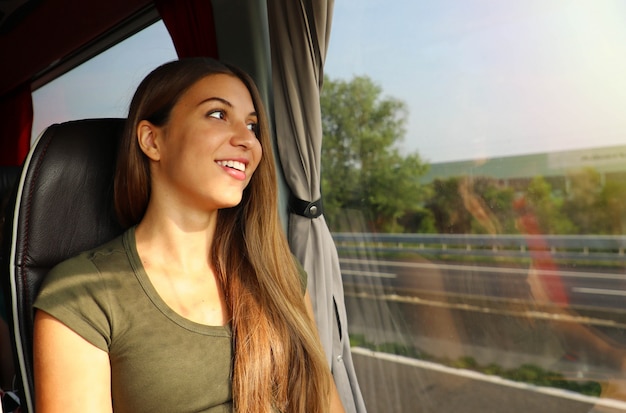 Mujer hermosa joven que mira por la ventana del autobús. Pasajero de autobús feliz viajando sentado en un asiento y mirando por la ventana.